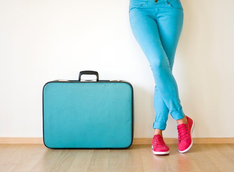 Young woman stands beside old fashioned suitcase, ready to travel f