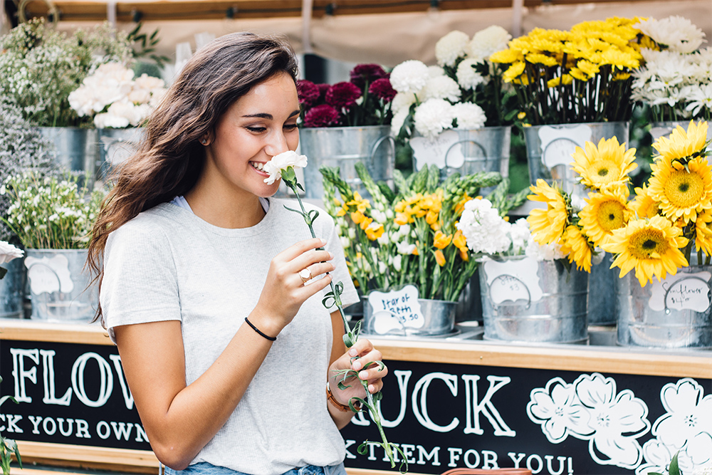 woman smelling carnations in front a flower stand