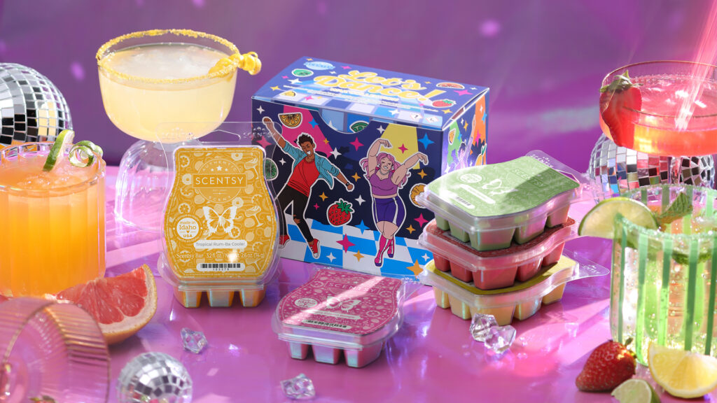 The Scentsy Let's Dance Wax Collection box and corresponding wax bars are displayed on a purple tabletop surrounded by confetti, fruity cocktail drinks, and party decorations. 