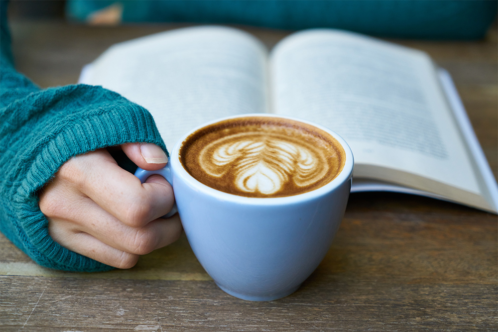 woman reading open book with coffee