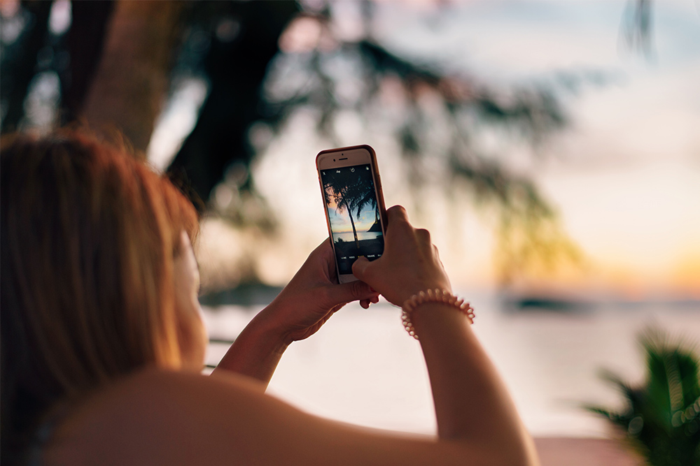 Photo of woman taking a photo of a beach with her phone camera