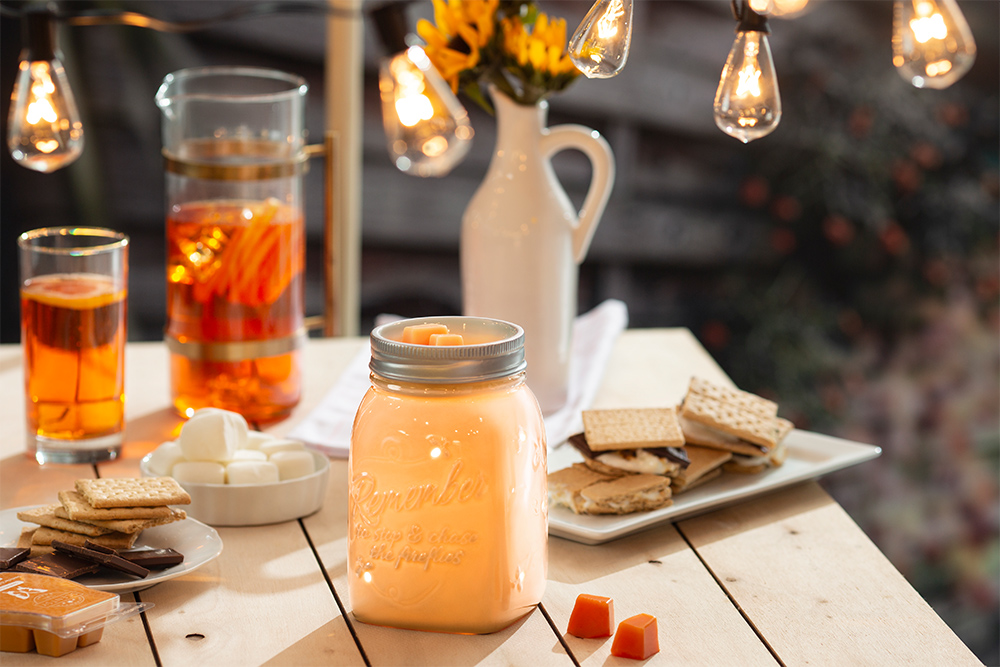 Photo of Scentsy's Chasing Fireflies Warmer atop a summery camp scene with smores