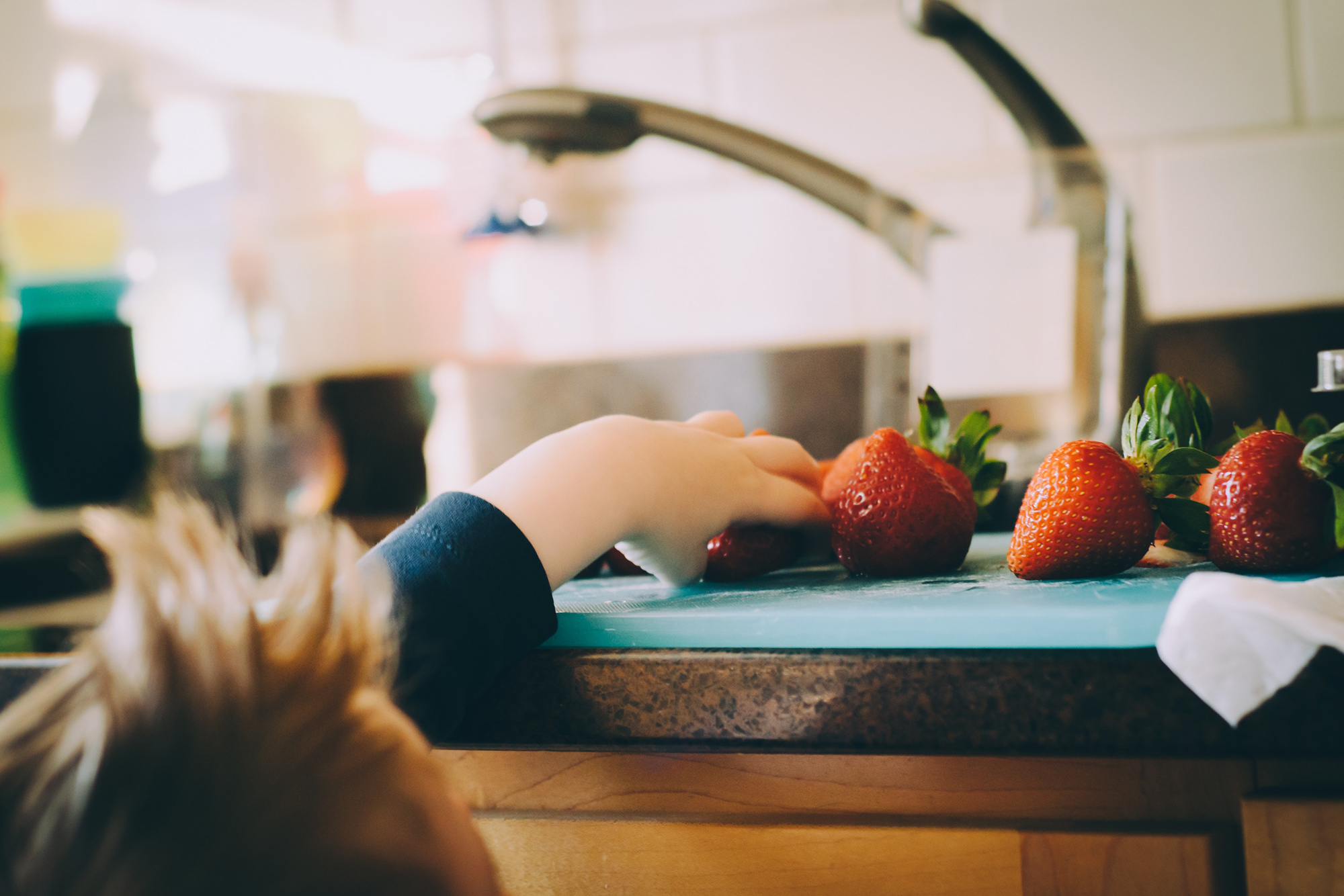 Little boy reaching up for strawberries in Kitchen