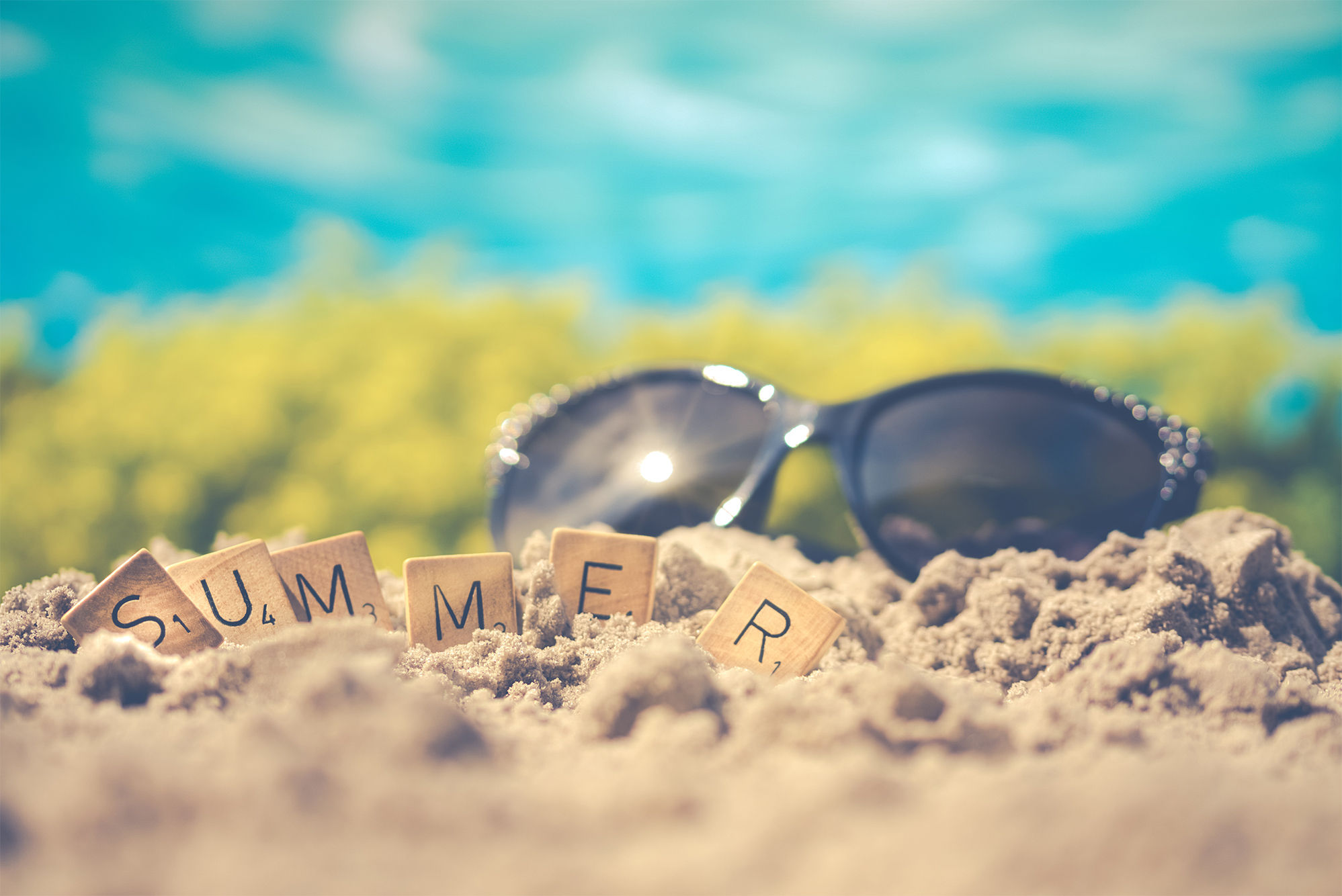 scrabble letters spelling out summer in the beach sand