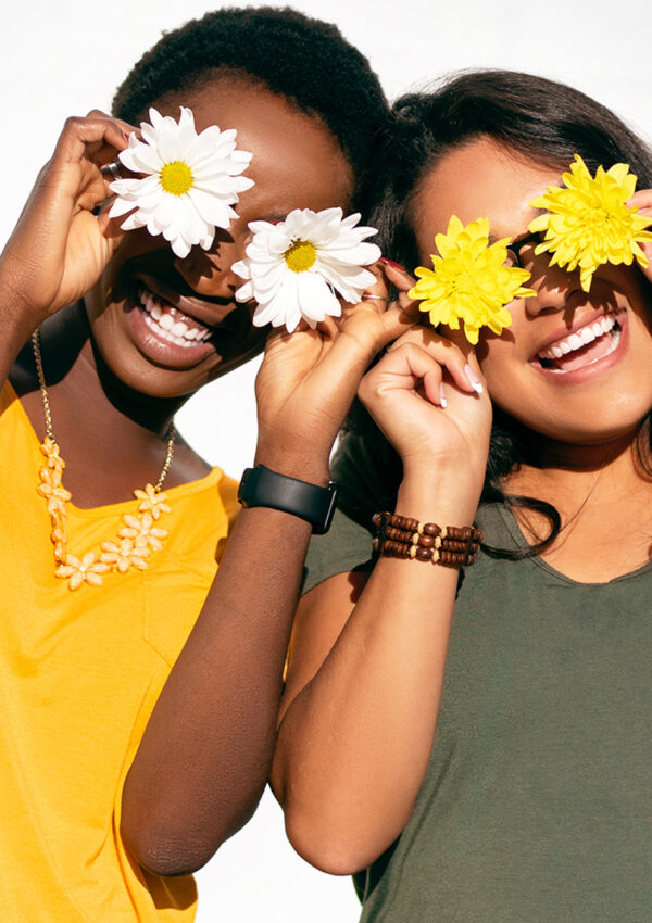 Girls holding flowers in front of their eyes while laughing