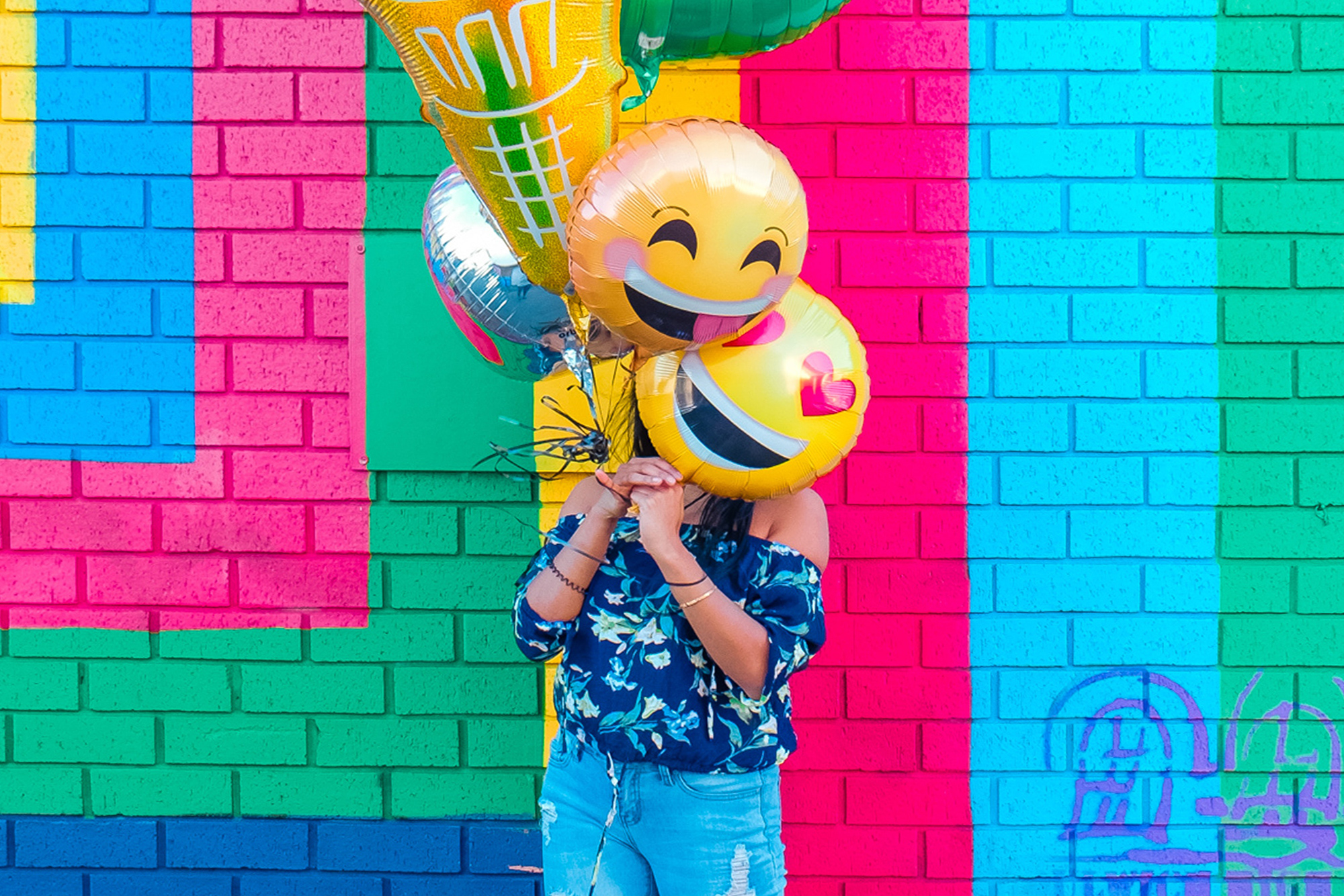 Woman holding emoji balloons in front of a colorful wall