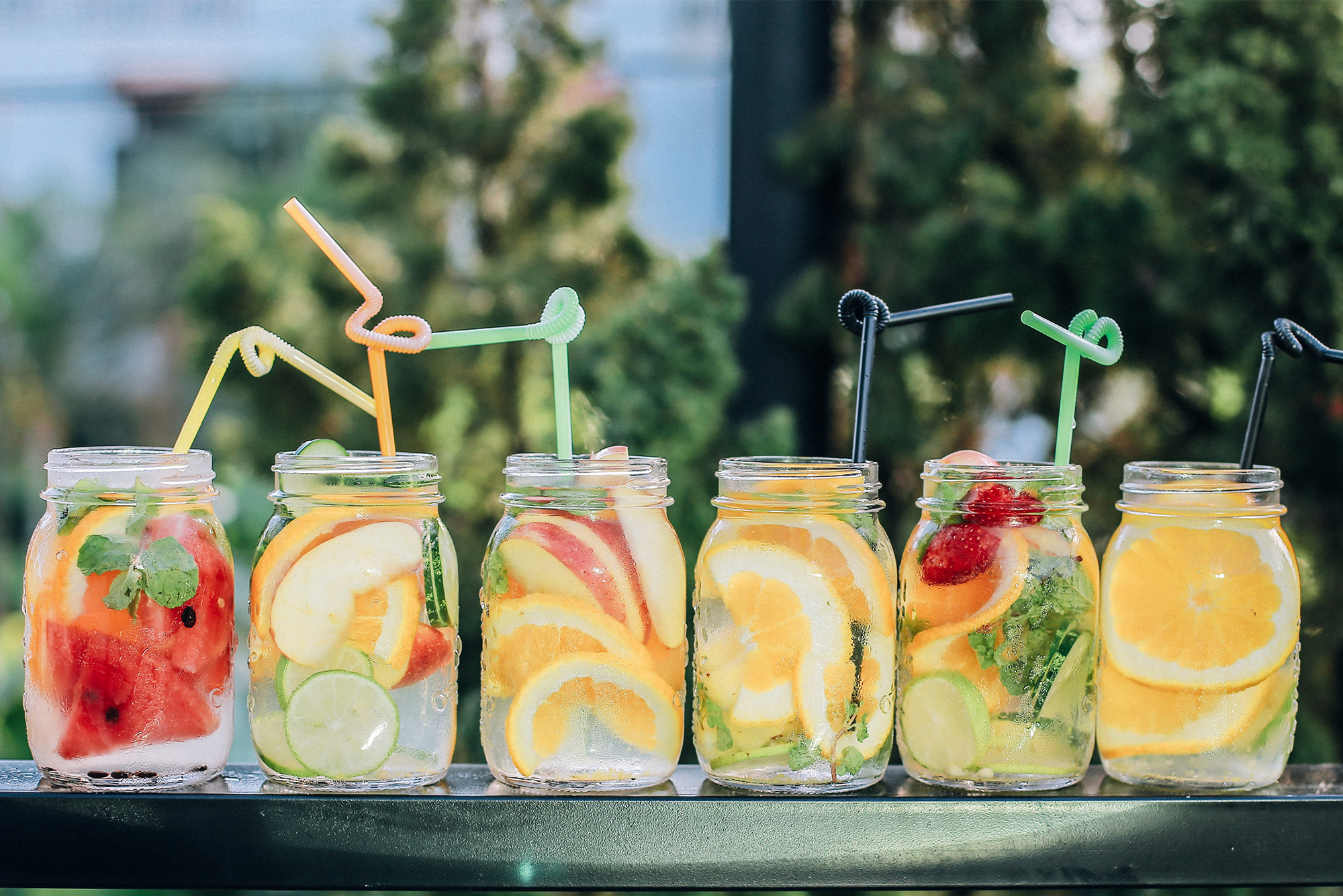 Six fruity drinks lined up on a fence