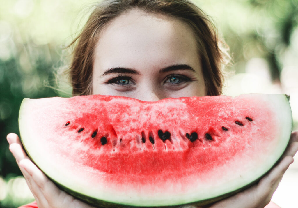 Woman holding a watermelon in front of her face as a smile