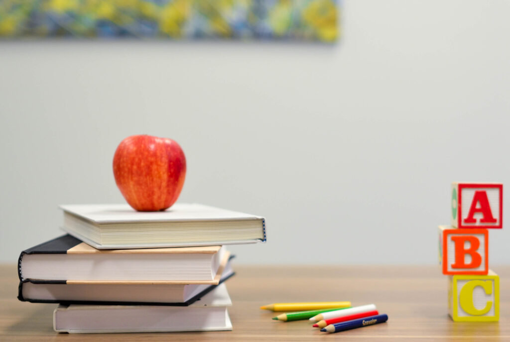 Apple on a stack of books with ABC blocks and pencils on a table