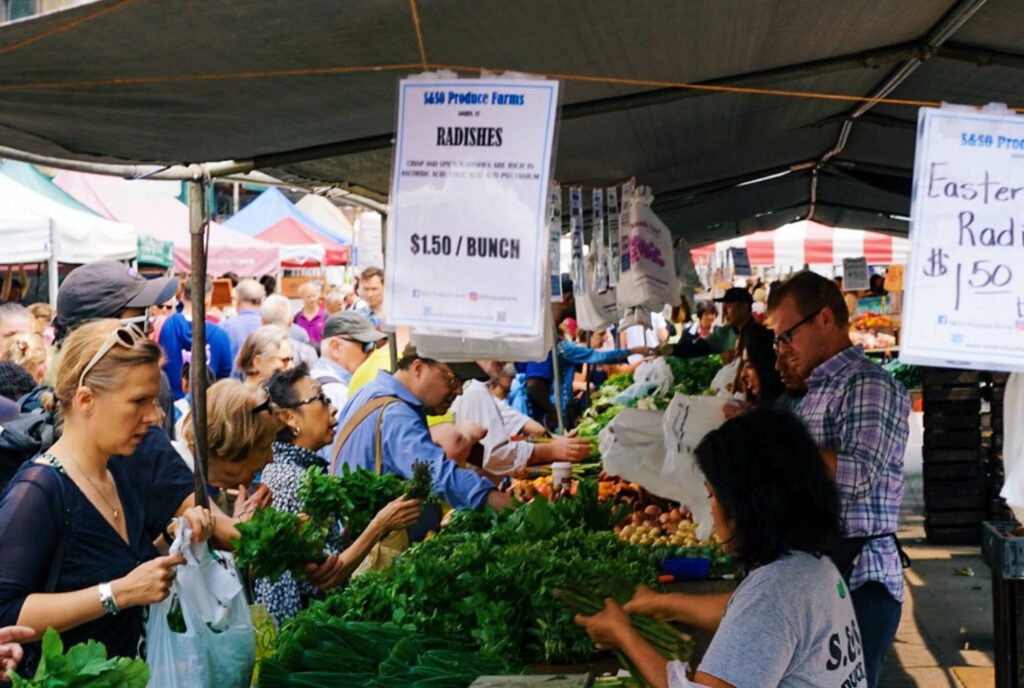 Woman shopping at a farmers market while lots of people move around in the background