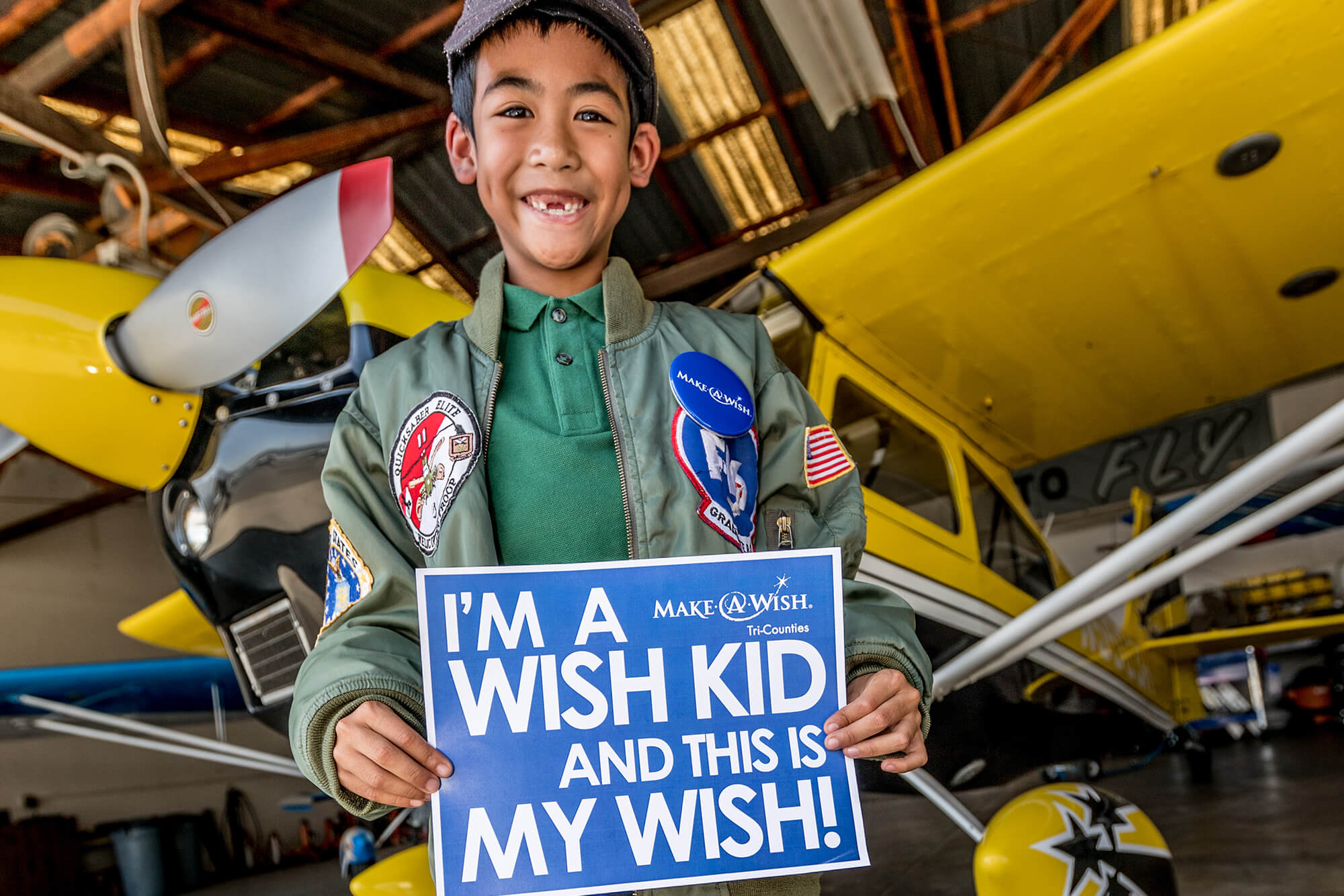 little boy holding a Make A Wish sign in front of plane