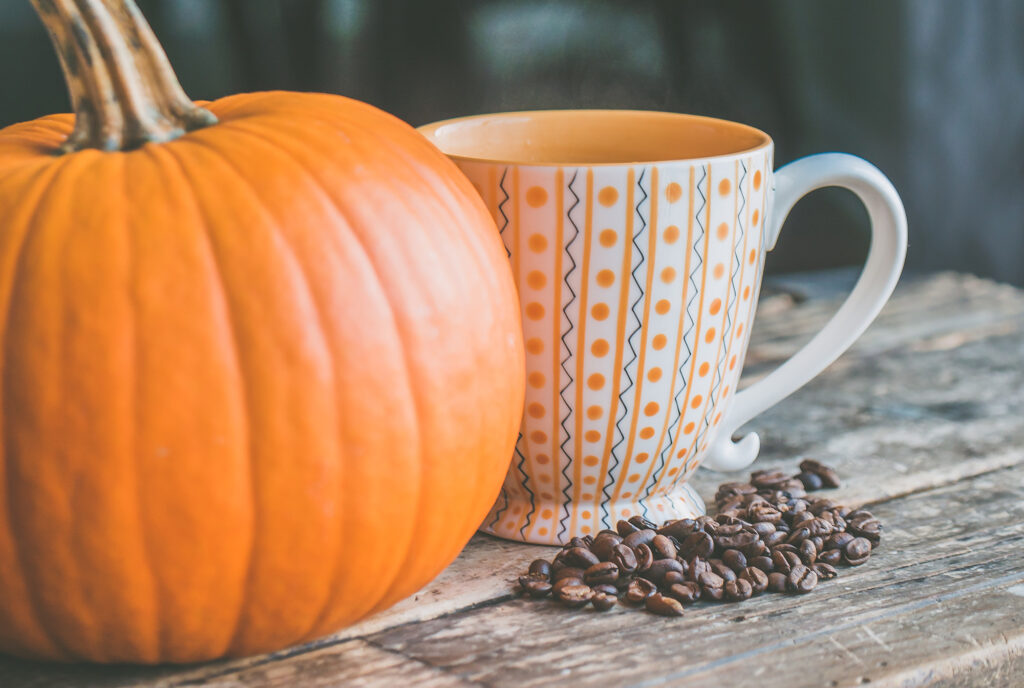 Pumpkin next to a coffee mug and coffee beans on the table