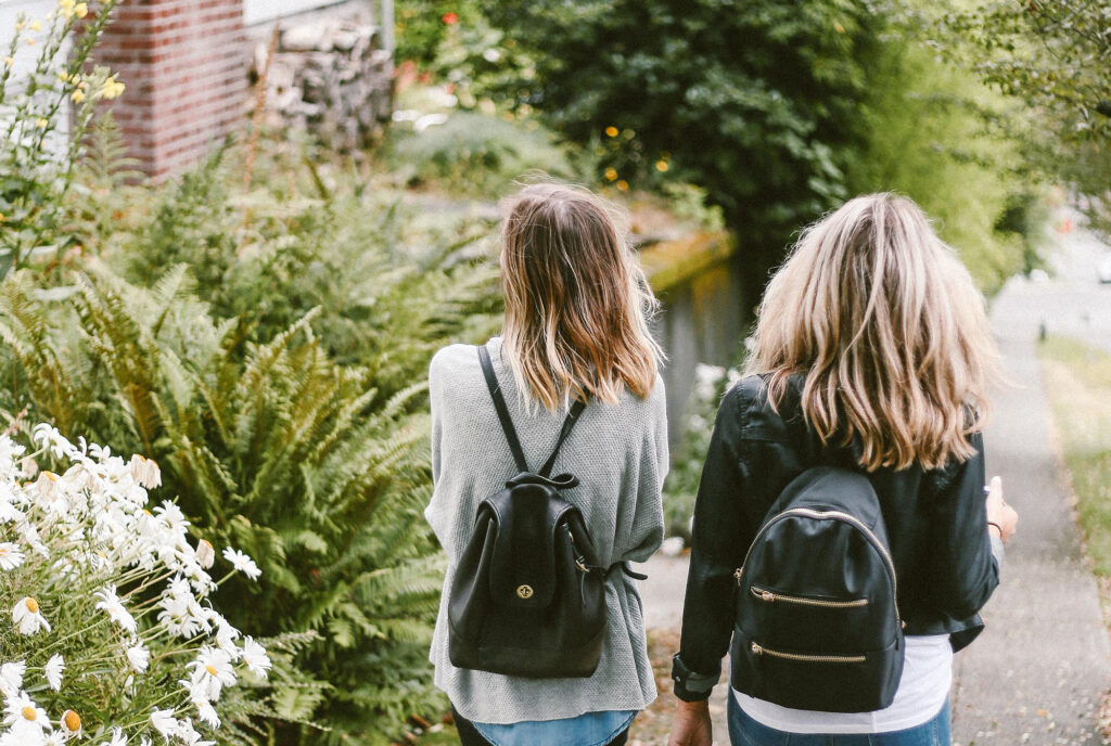 Two women walking down the sidewalk next to some bushes