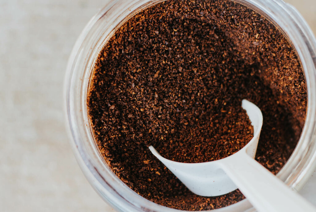 Measuring cup in a bowl full of coffee grounds