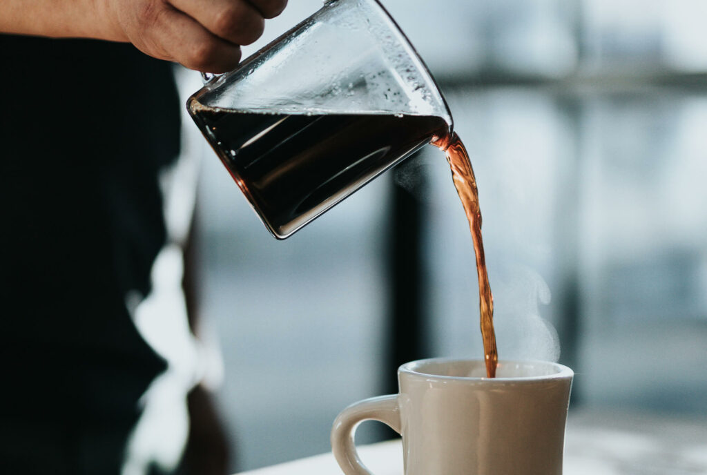 Person pouring black coffee into a ceramic mug