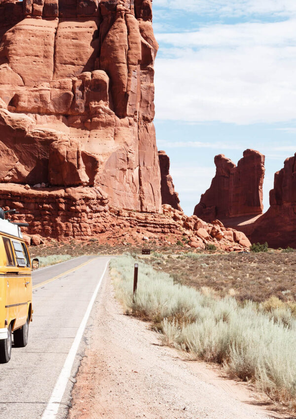 Yellow van driving on highway with giant rock structures and a brush field
