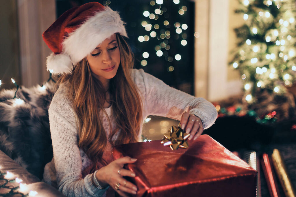 Woman wearing Santa Claus hat putting a bow on a wrapped present