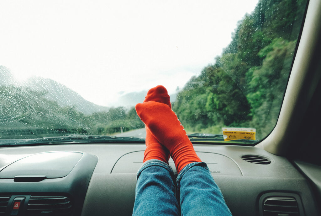Passenger in car resting their feet on the dashboard of a car while on a road trip