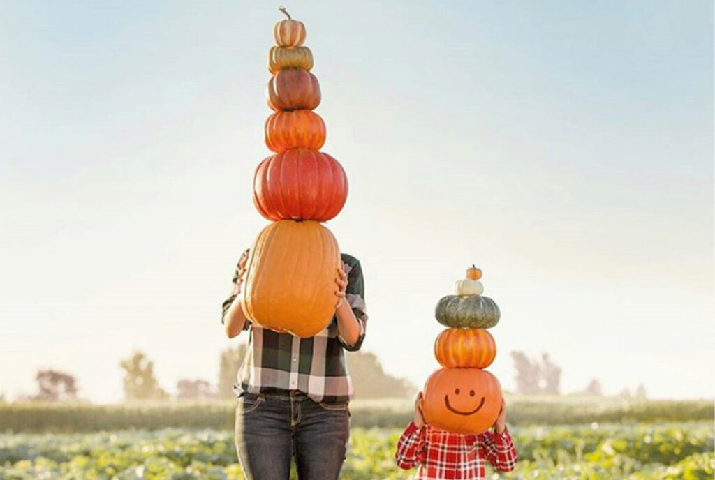 Woman and child holding a stack of pumpkins