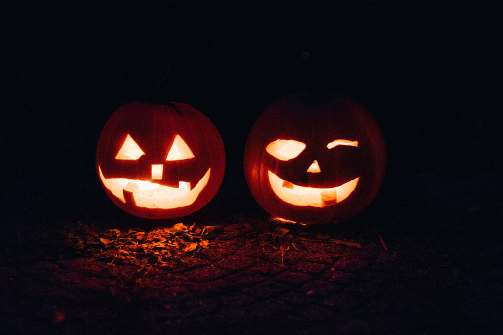 two carved pumpkins glow with goofy faces in the night