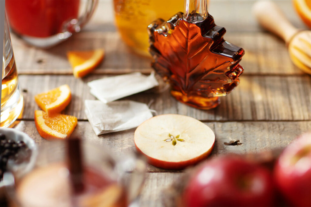 Glass of maple syrup next to a sliced apple round and more ingredients