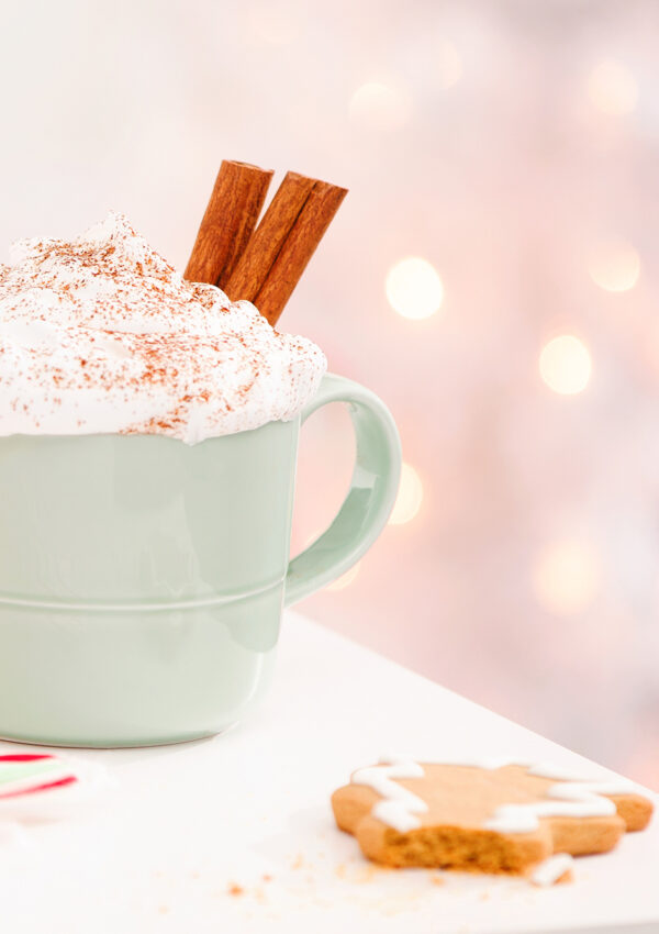 Hot chocolate in a ceramic mug with whipped cream and cinnamon sticks and a partially eaten gingerbread man