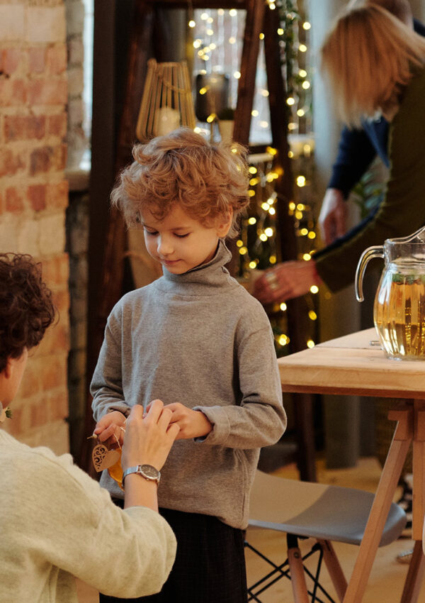A little boy being handed an ornament by an adult male to hang up on the tree beside a table set for holiday feast with christmas decor all around