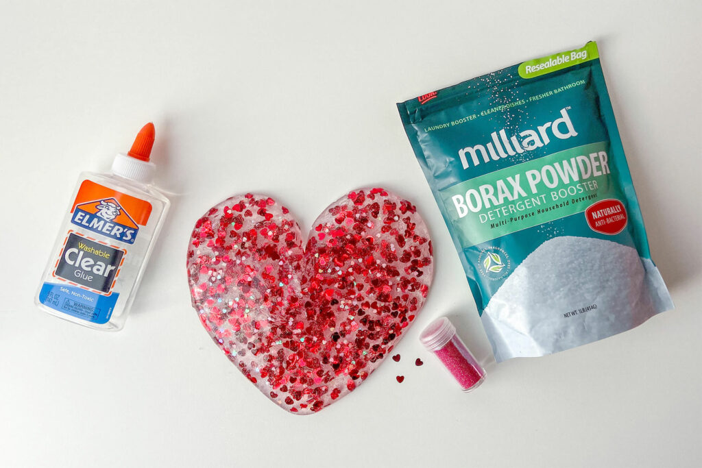Valentine's Day slime in the shape of a heart surrounded by Elmer's Clear Glue, Borax, and hearts glitter