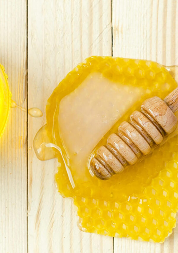 Jar of honey next to a honey dipper resting on a honeycomb