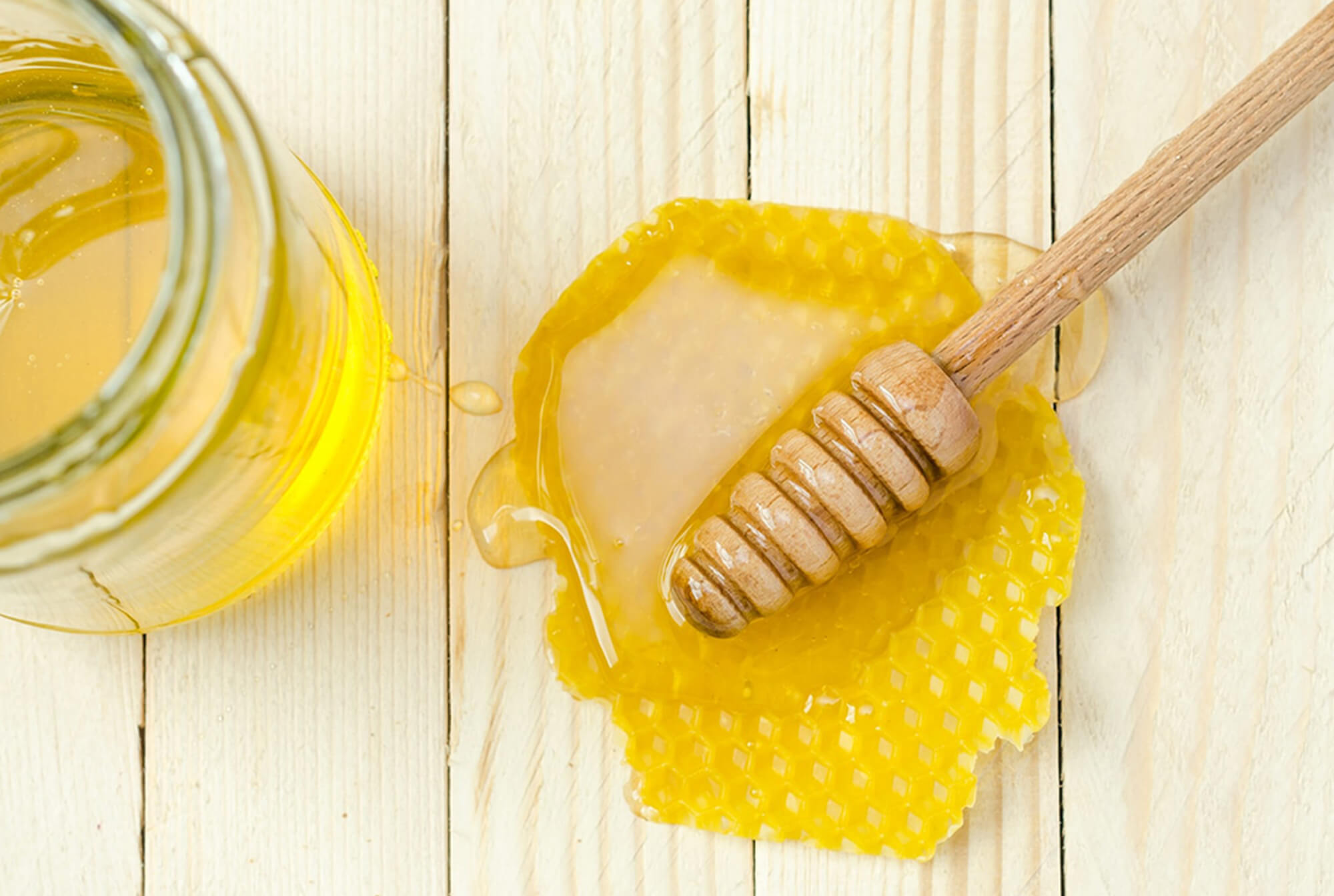 Jar of honey next to a honey dipper resting on a honeycomb
