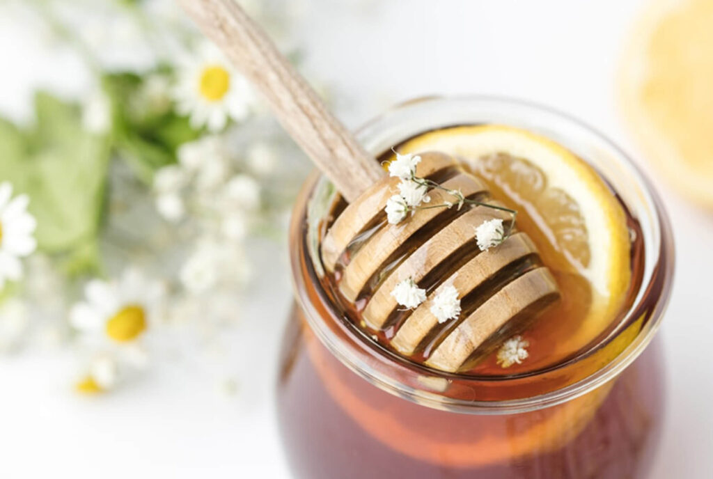 Honey dipper in a small jar of honey with flowers around it