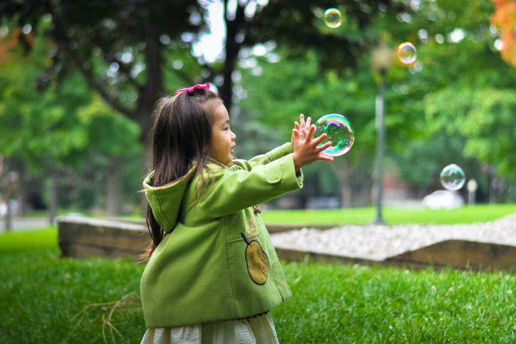 Little girl reaching for a bubble in an empty park