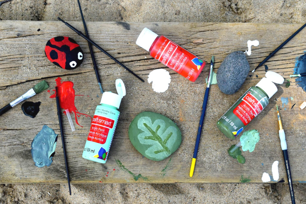 Rocks painted to look like a ladybug and a leaf surrounded by art supplies