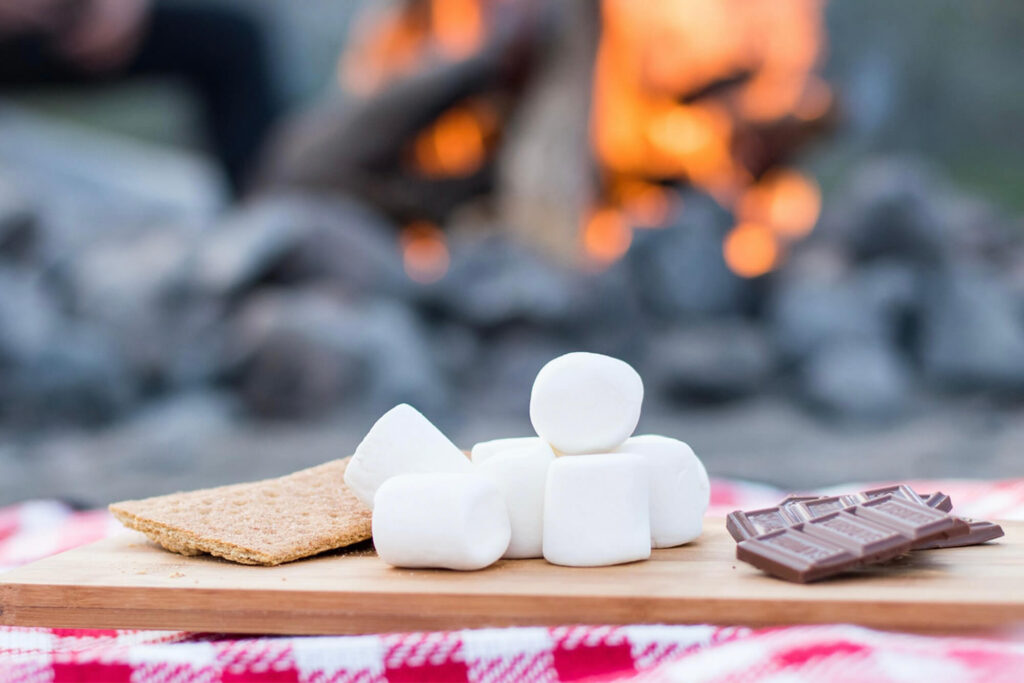 Graham crackers, marshmallows and chocolate on table next to fire