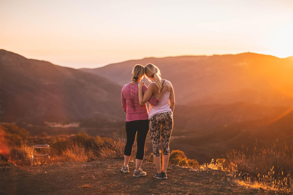 Two women supporting each other while watching a beautiful mountain top sunset