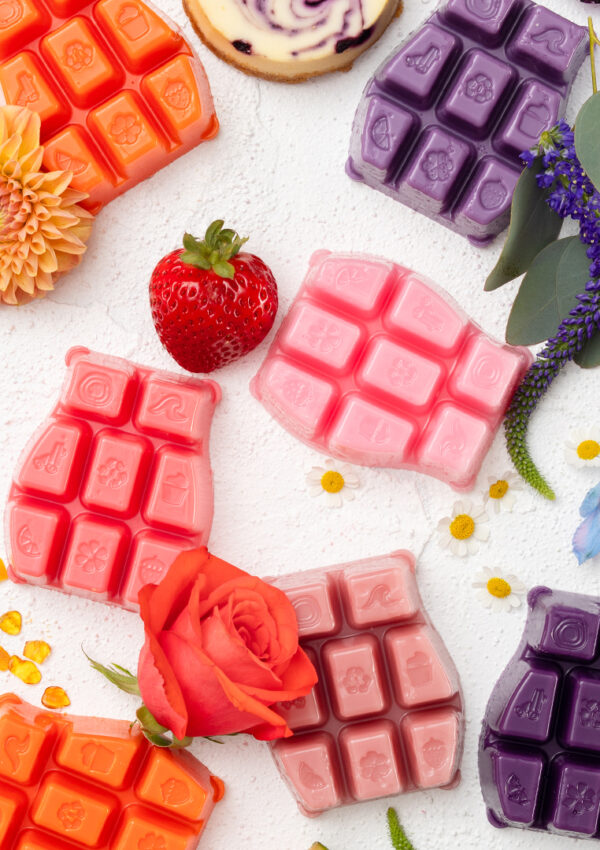 A top-down view of Scentsy wax bars in a variety of colors spread out among fragrance notes associated with the different wax bars.