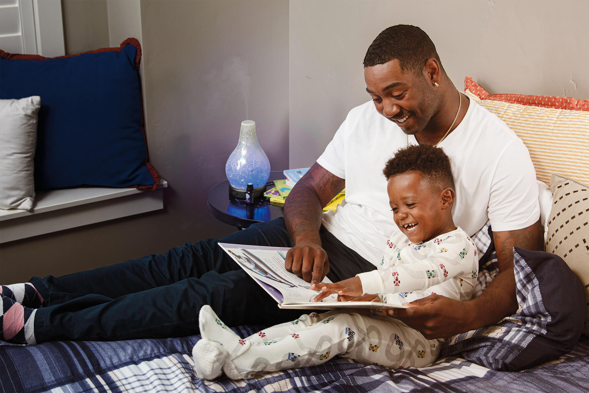 Father reading story to son while laying in bed with a Scentsy diffuser on a bedside table