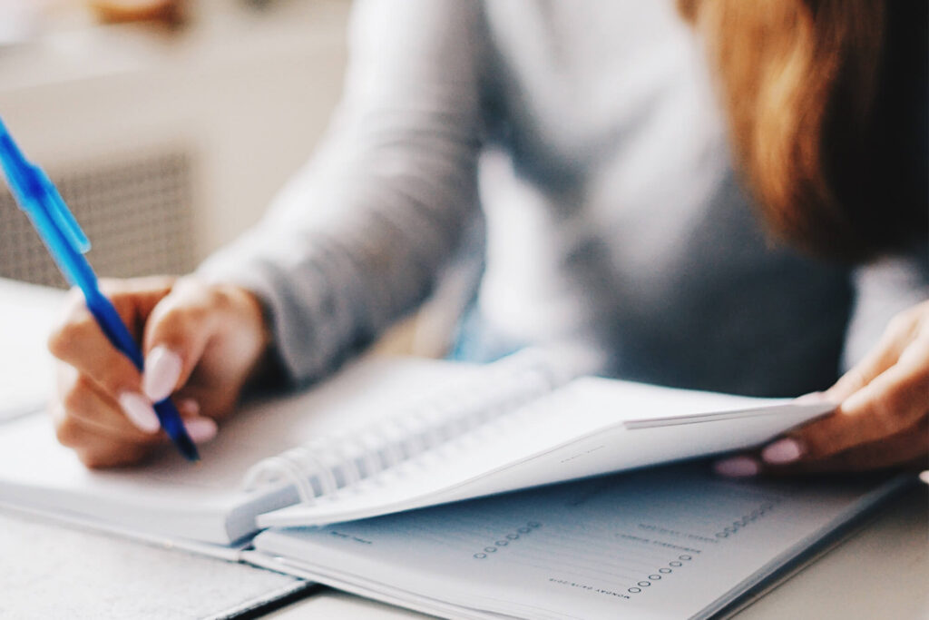 Person writing in a notebook with a blue pen