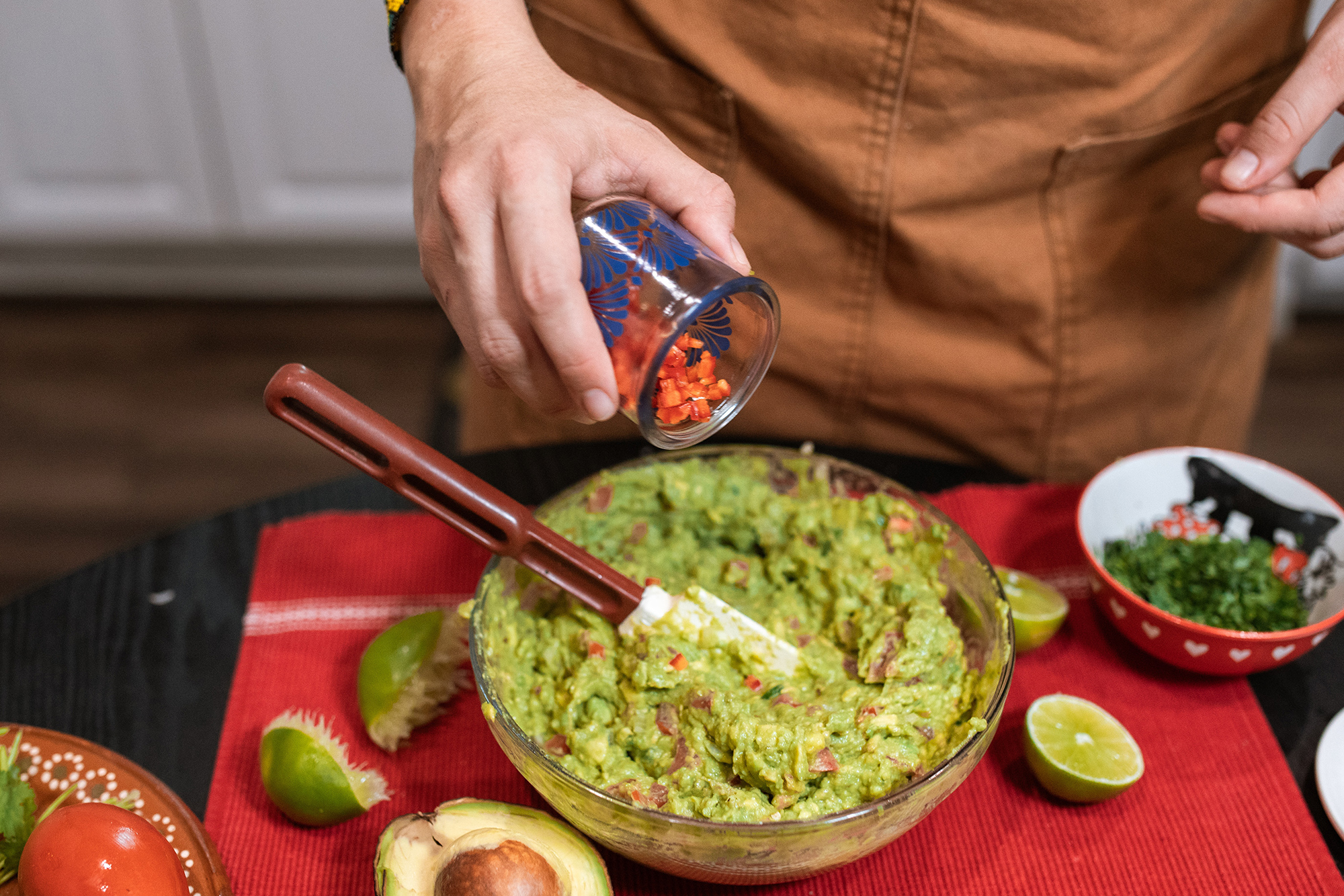 Person making guacamole with ingredients surrounding the bowl
