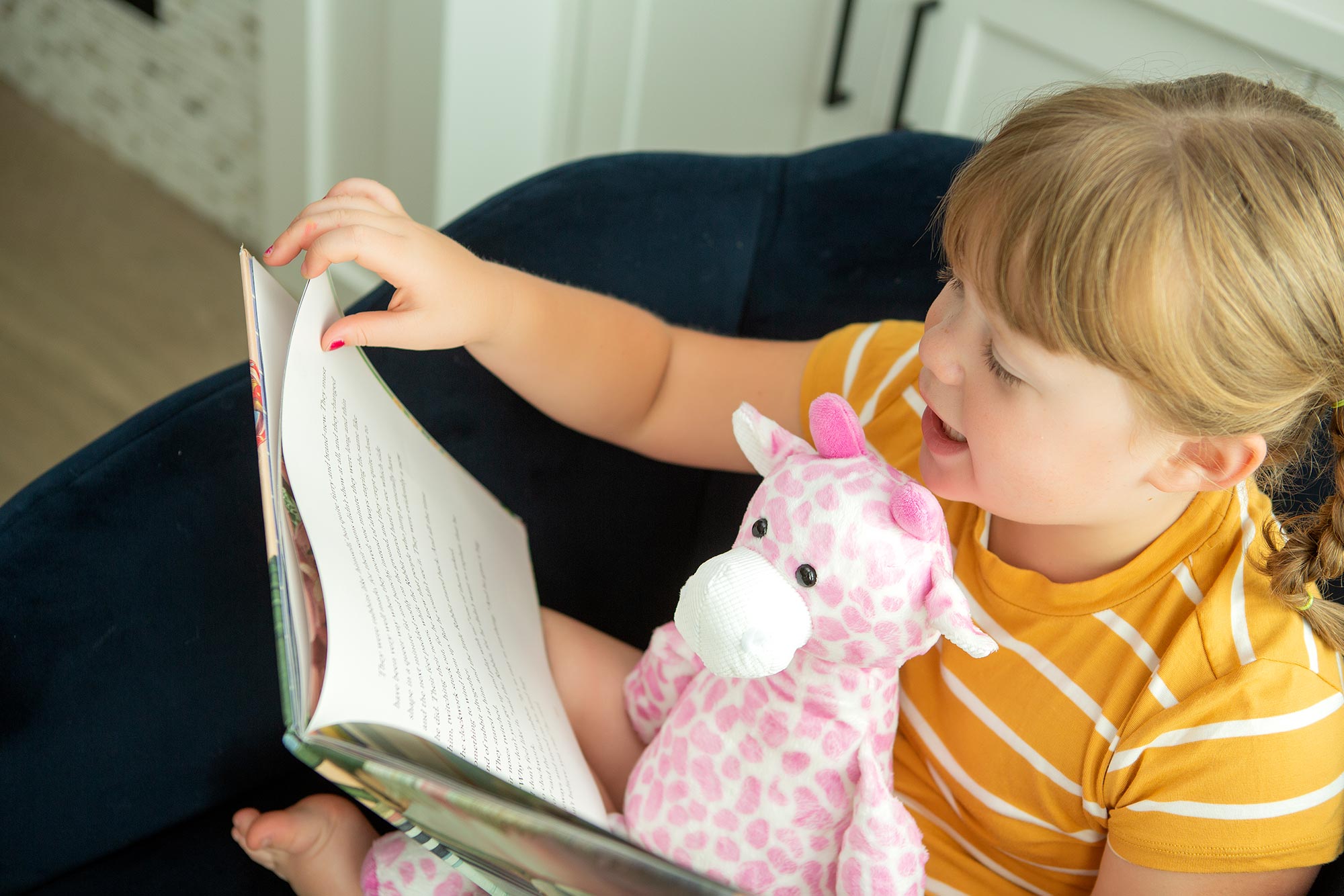 little girl reading book with pink giraffe Scentsy Buddy in her lap