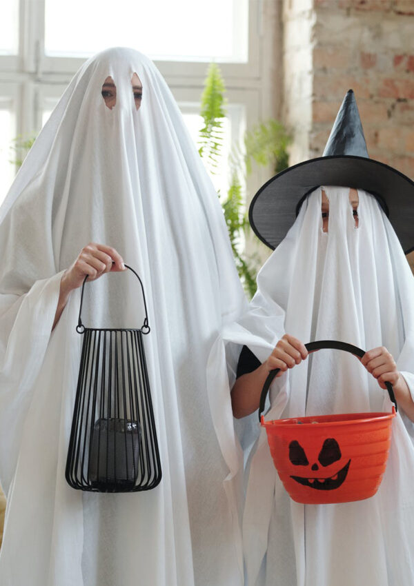 Two people dressed up as ghosts both holding bags for candy
