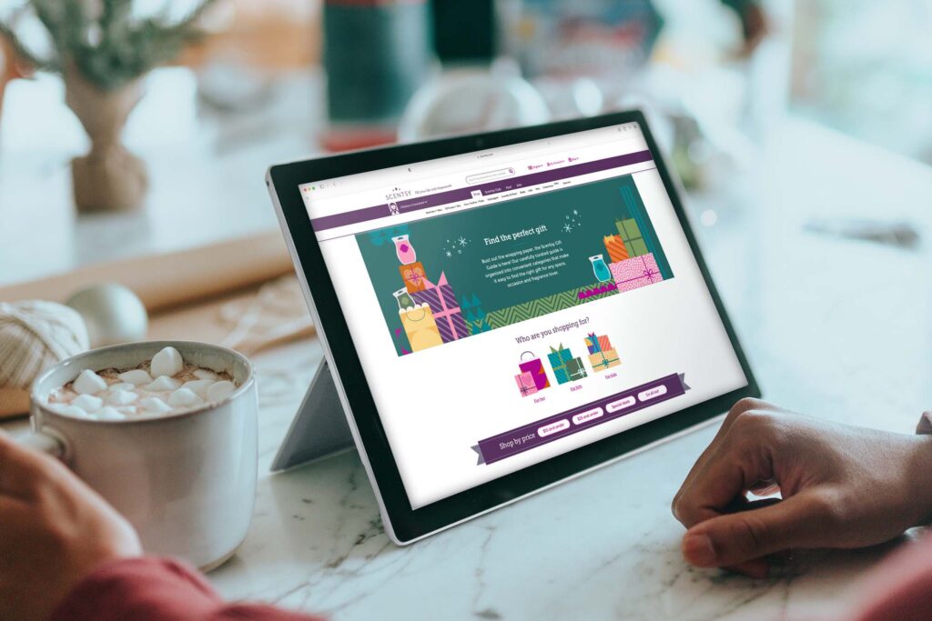 Scentsy homepage pulled up on an iPad while a person looks at the screen with a mug of hot cocoa in their hand