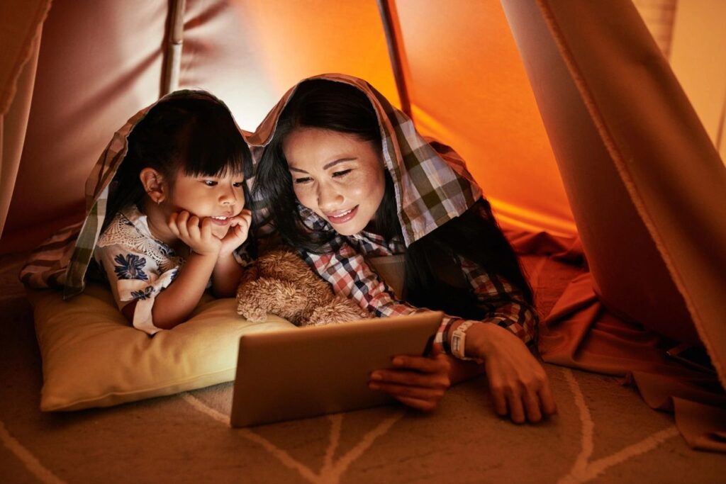 Mother and son in a fort built with sheets watching a movie