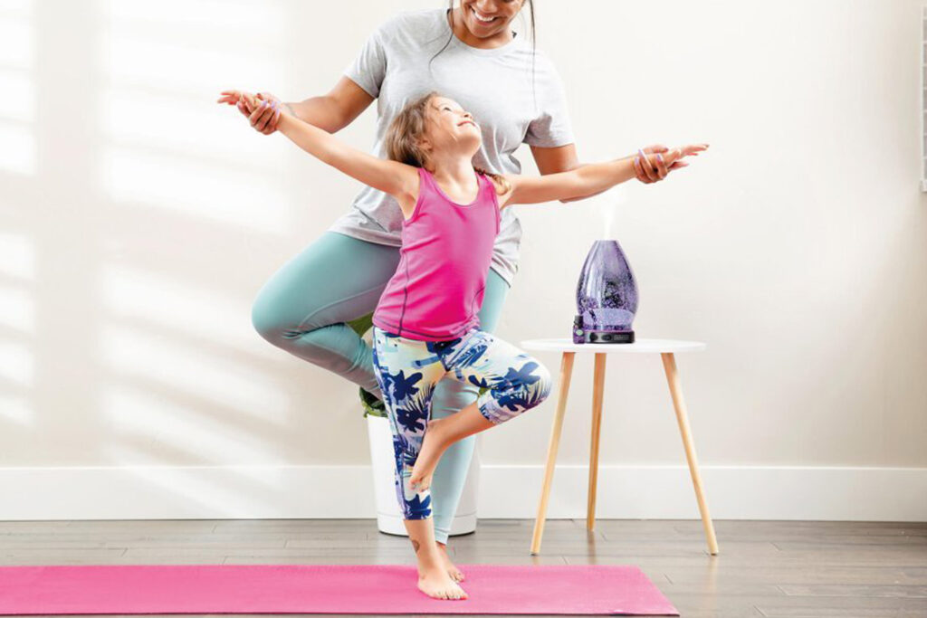 Mom and daughter doing a pose on a yoga matt with a Scentsy Oil Diffuser giving off fragrance on a small white table