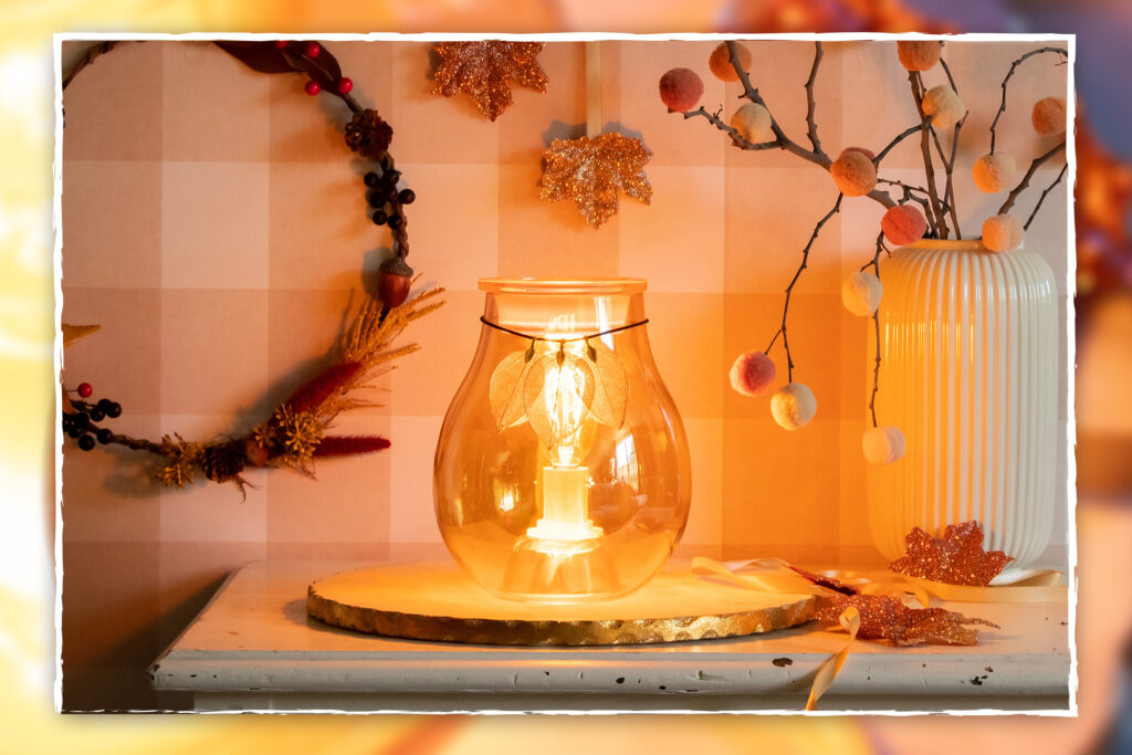 DIY pom pom branches which are small tree branches with pom poms glued all over to look like flowers sitting in a vase with the glittery leaf garland and homemade autumn wreath both hanging on the wall! Next to all of the fall inspired crafts is the Amber Glow Scentsy wax warmer lit up