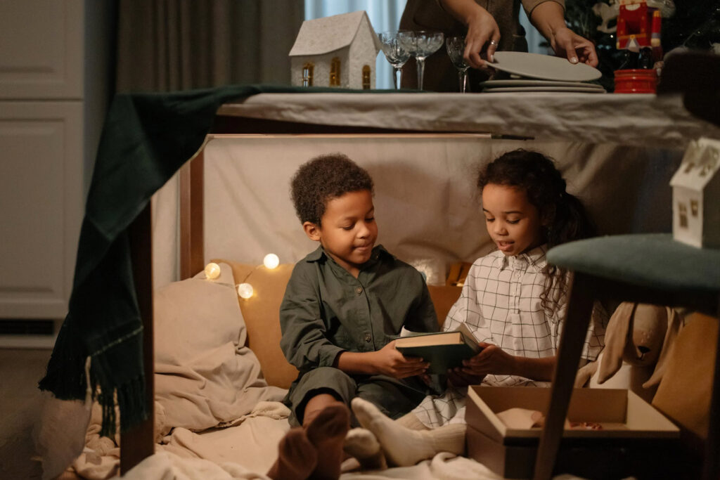 Two kids in a blanket fort reading a book