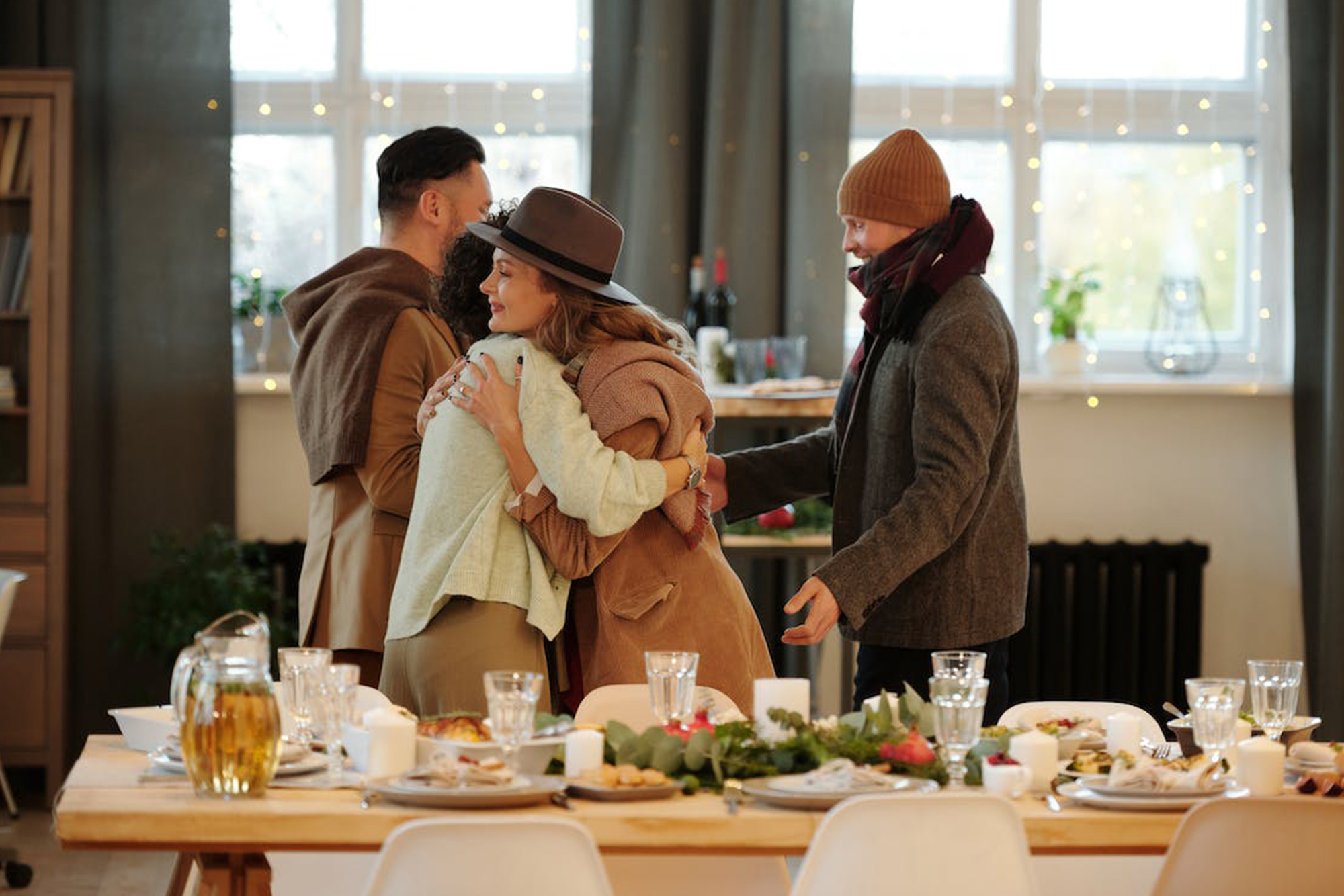 Four people embracing each other with hugs and handshakes around the dinner table at a holiday party