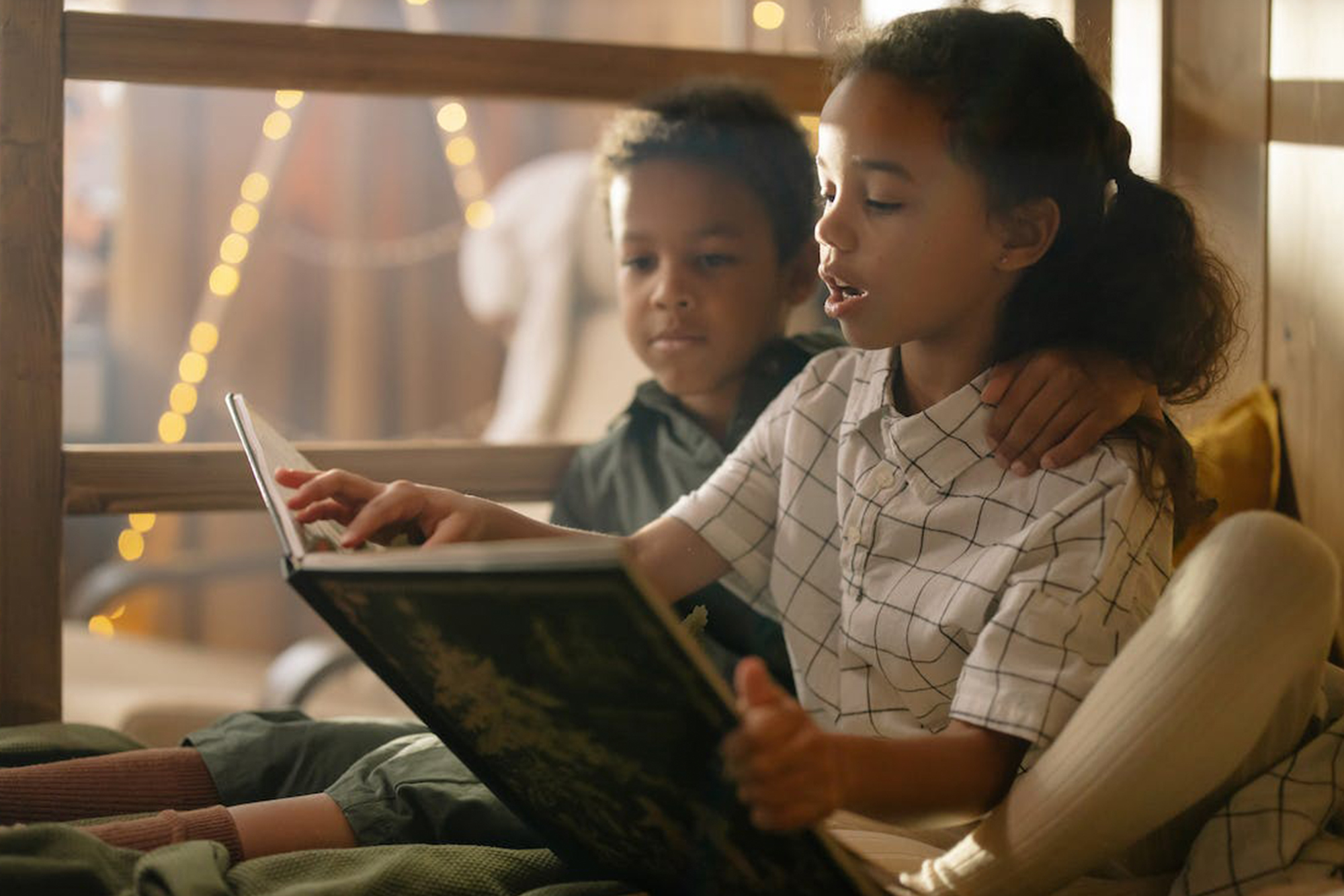 Older sister and younger brother sitting in bed reading a Christmas story