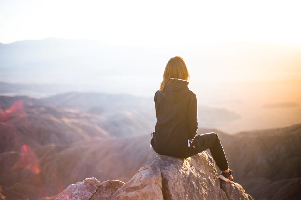 Girl on a hike sitting on the top of a mountain overlooking the mountain range and ocean 