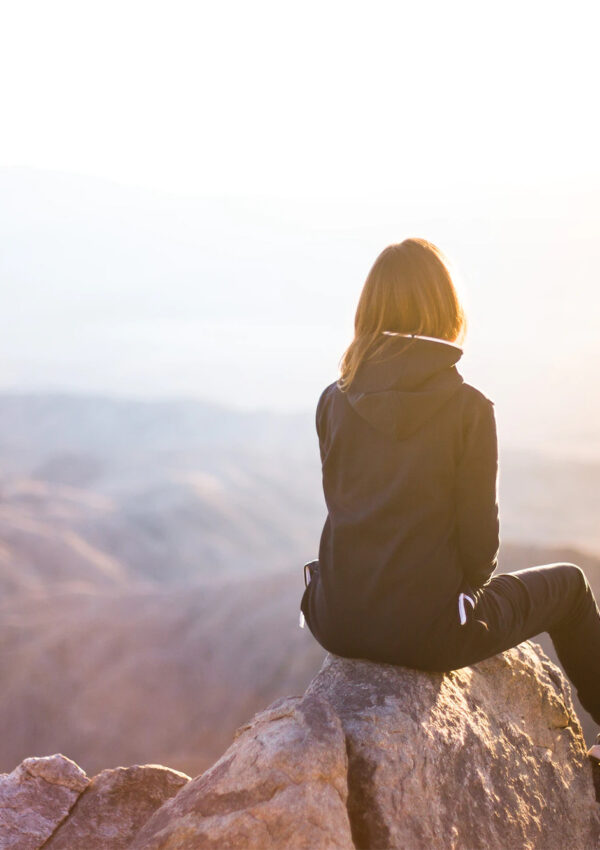 Girl on a hike sitting on the top of a mountain overlooking the mountain range and ocean
